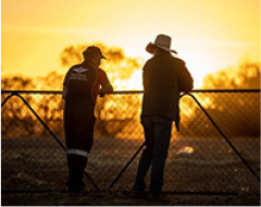 A RFDS staff member and a man standing behind a fence, silhouetted against a vibrant sunset sky.