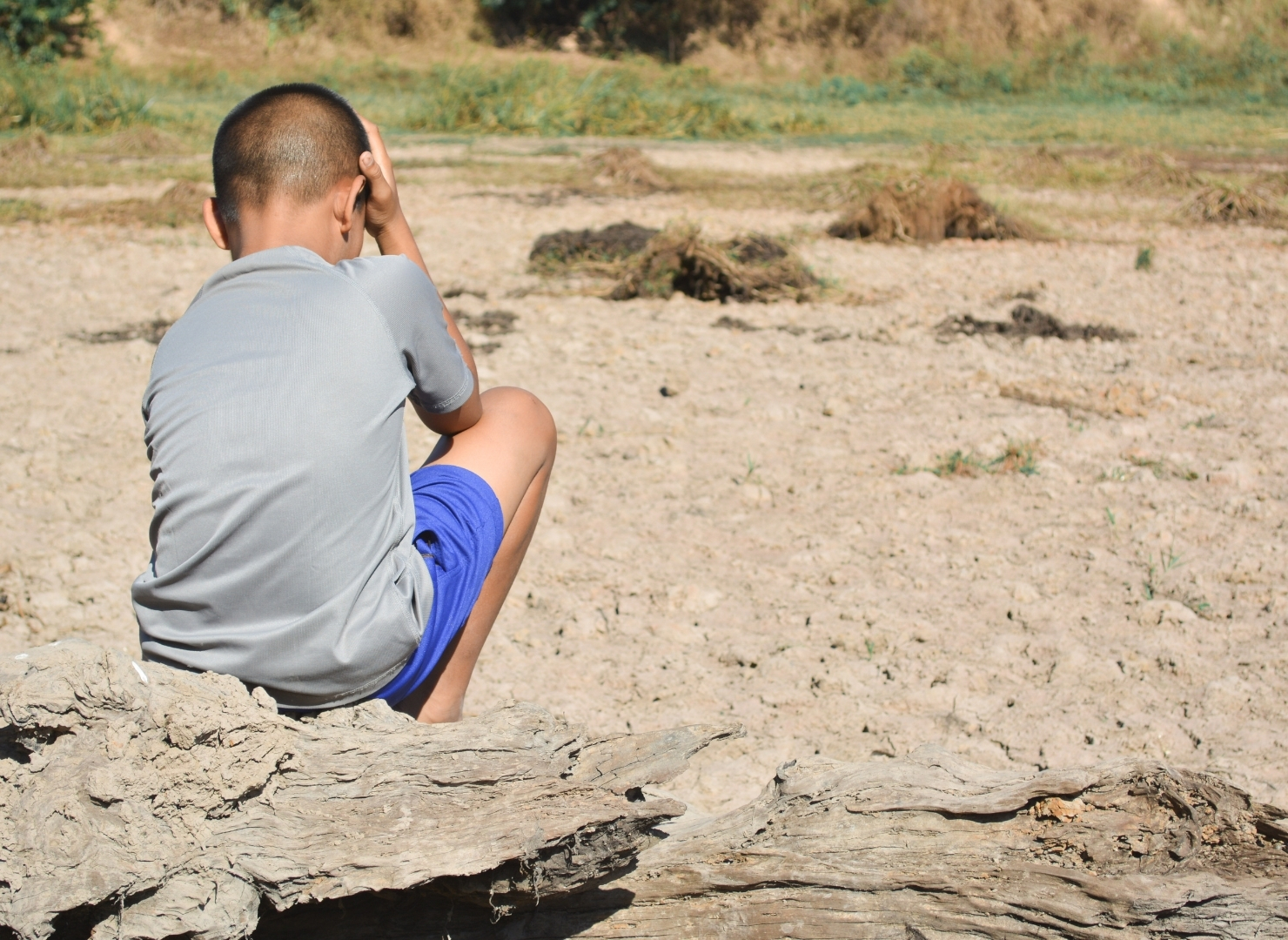 A young boy sits on rocky ground in a dry beach flat, facing away from the camera.
