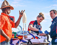 two paramedic assisting an individual on a stretcher bed, with the help of a farmer.